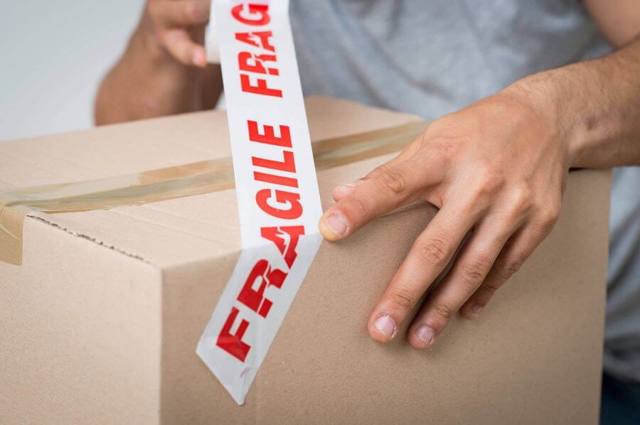 A man wrapping a cardboard box with the 'fragile' tape