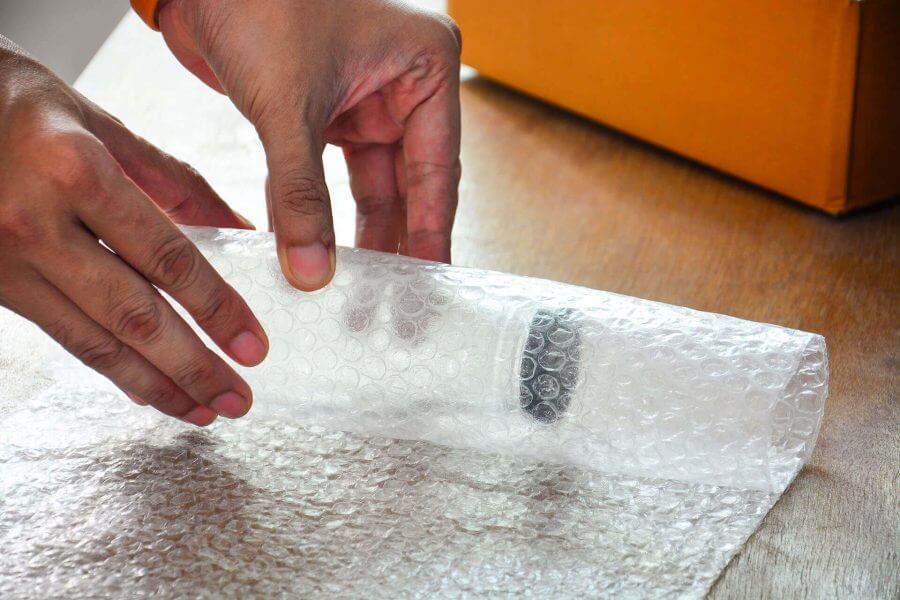 A person wrapping a bottle in bubble wrap