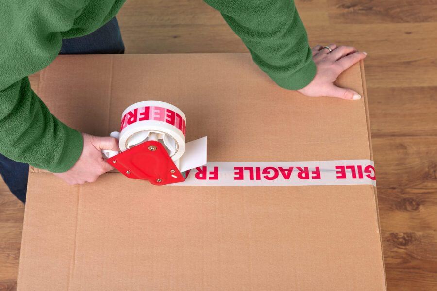 A woman putting a fragile tape over a cardboard box