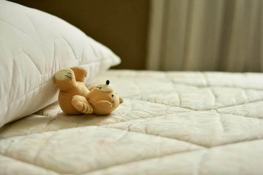 An image of a mattress, pillow, and a teddy bear
