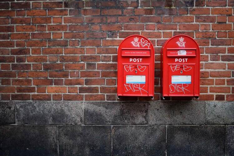Two red mailboxes hanging next to each other on a brick wall