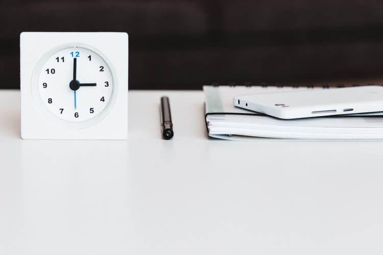 A clock, notebook and phone placed neatly on a white surface