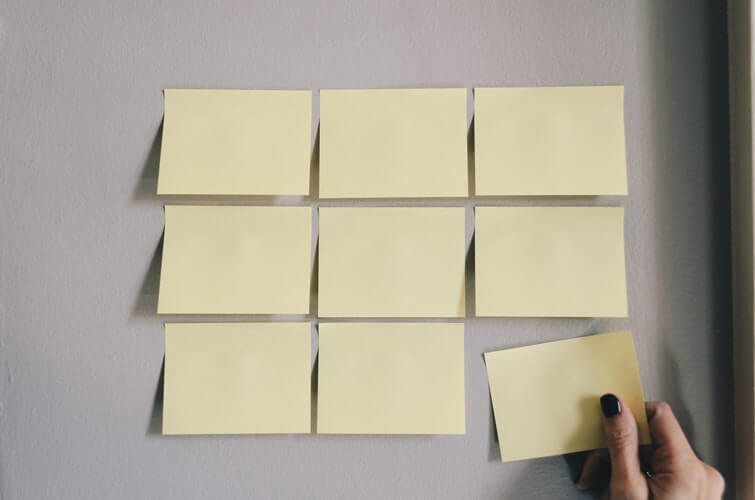 A bunch of sticky notes on a wall, and a person tearing one away