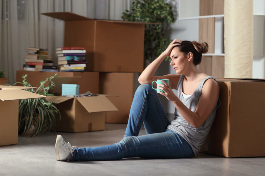 A stressed woman sitting on the floor holding her head surrounded by boxes