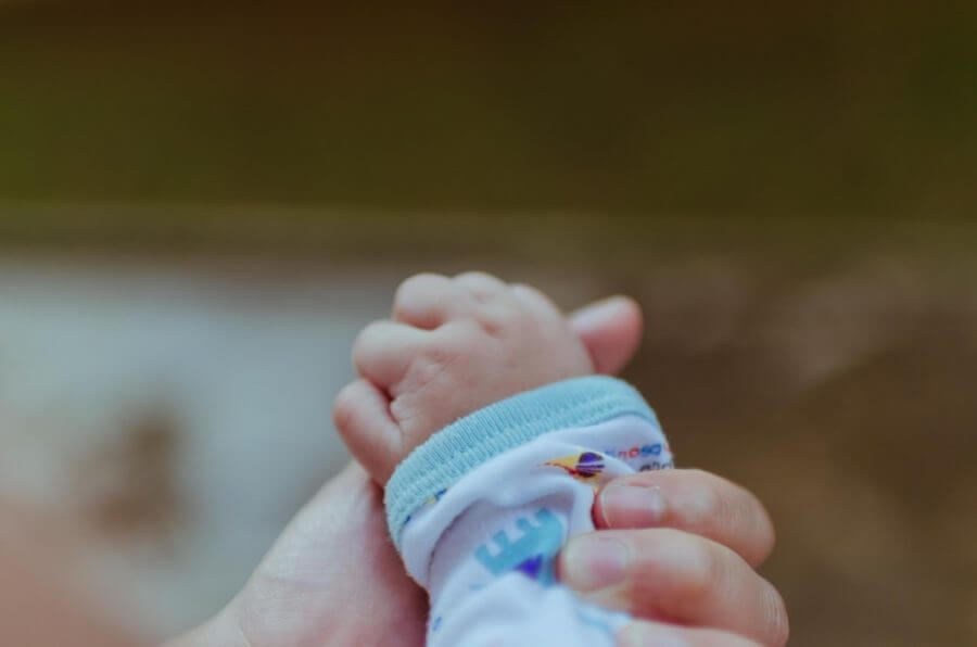 A parent holds baby’s tiny hand while long-distance moving