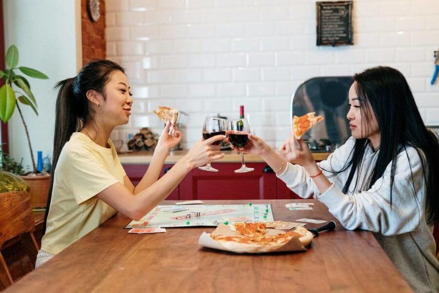 Two girls eating pizza and drinking wine before long-distance moving
