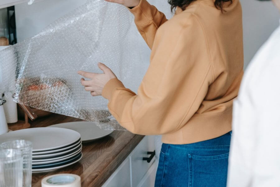 a woman wrapping up plates into bubble wrap, preparing for long-distance moving  