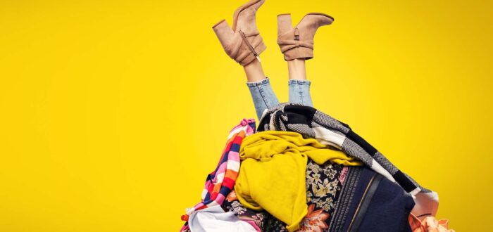 woman legs out of clothes pile on yellow background with copy space