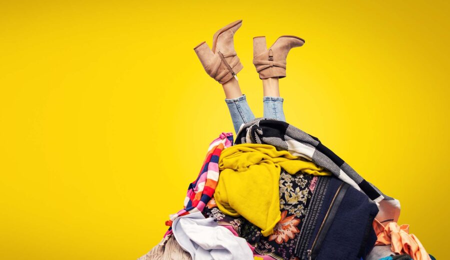 woman legs out of clothes pile on yellow background with copy space