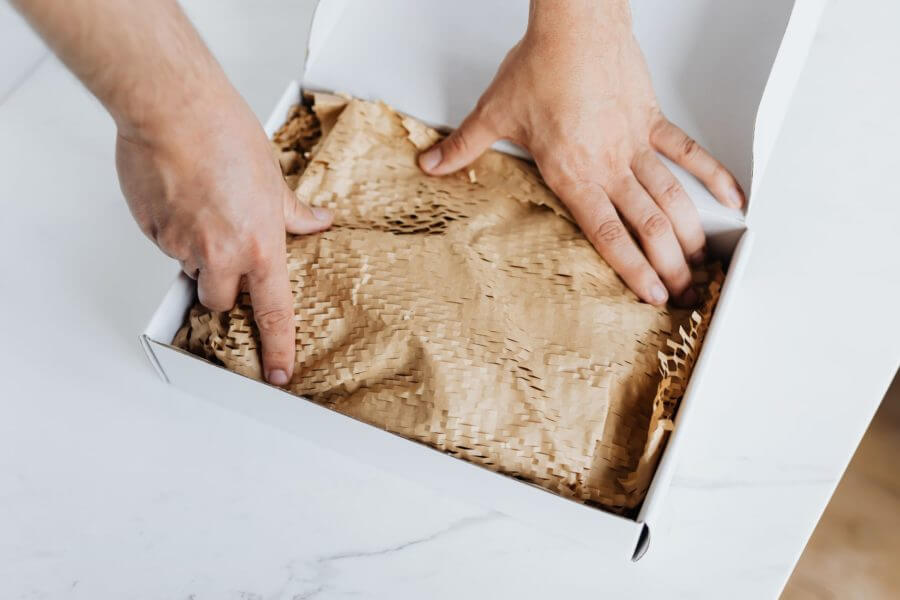 A person putting something into a white box wrapped in brown paper