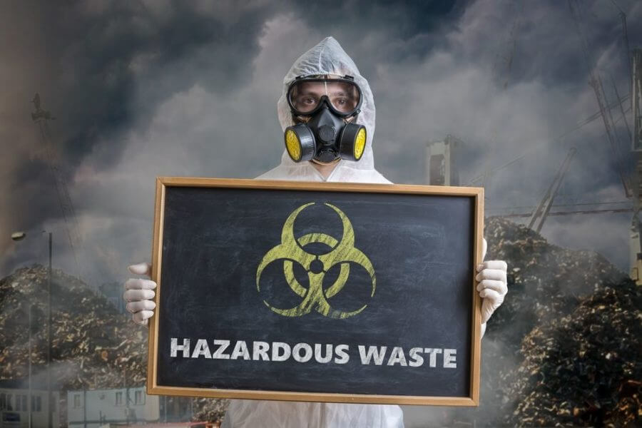 A man in protective gear holding a sign for hazardous waste
