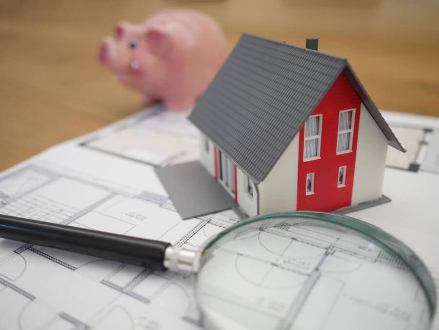 A model of a house on top of house plans and a piggy bank behind