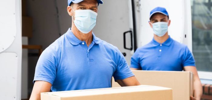 Professional cross-country movers wearing masks while carrying boxes