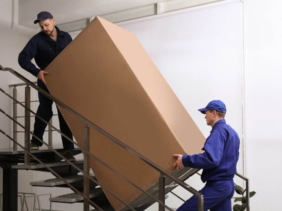 Cross-country movers carrying a large box up the stairs