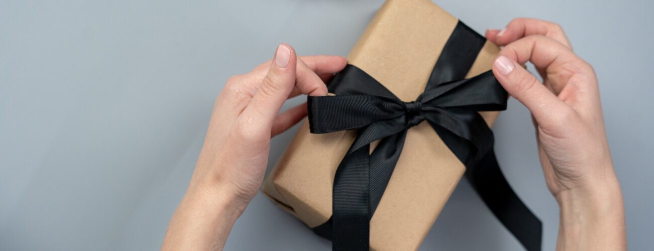 A person wrapping a gift with a black ribbon