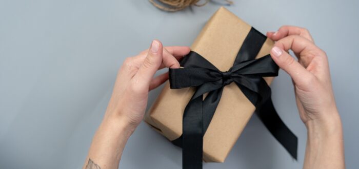 A person wrapping a gift with a black ribbon