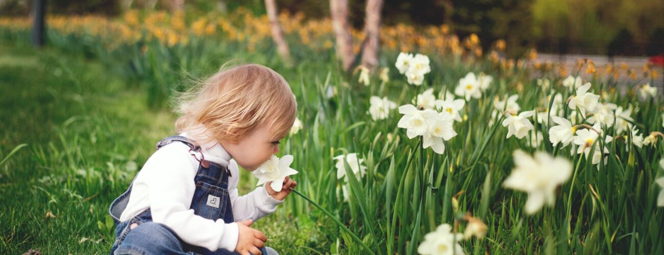Girl sitting on grass smelling white petaled flower
