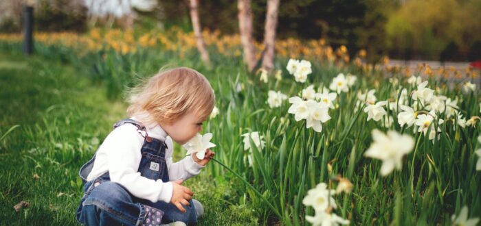 Girl sitting on grass smelling white petaled flower