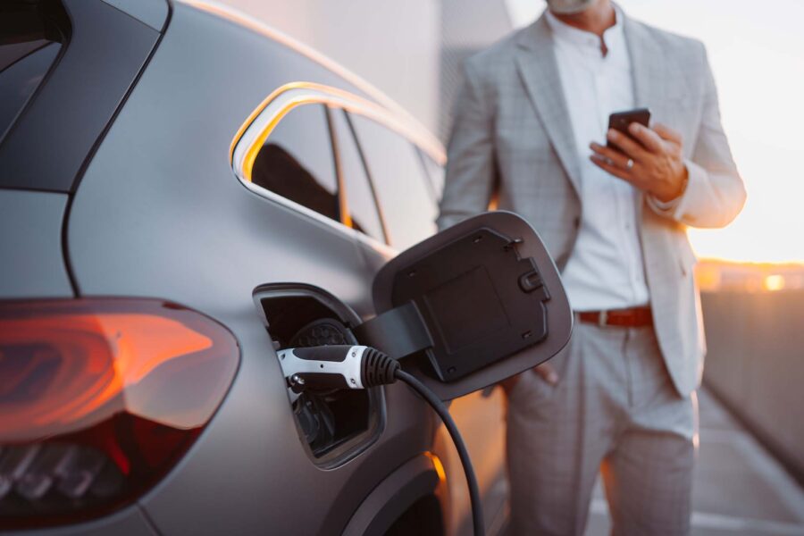 A man with a phone standing next to an electric vehicle being charged