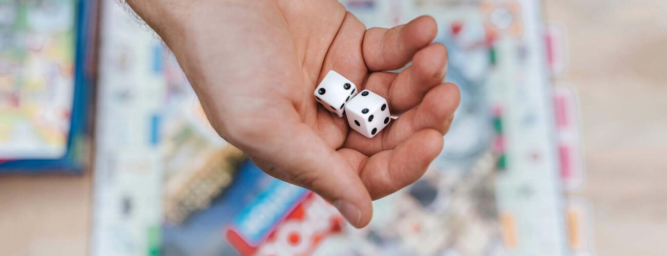 A person holding dice in their hand above Monopoly