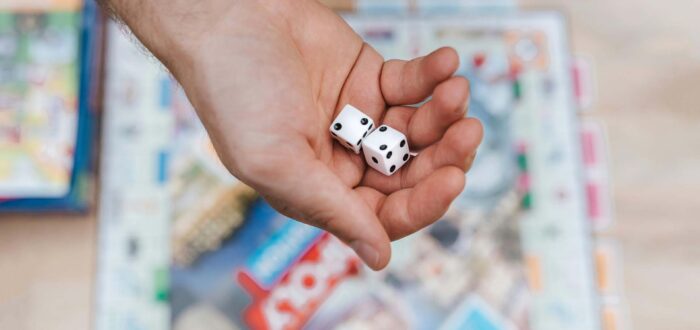 A person holding dice in their hand above Monopoly