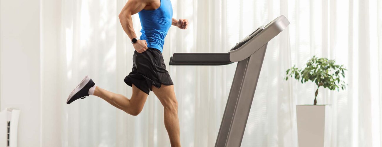 Full length profile shot of a young man running on a treadmill at home