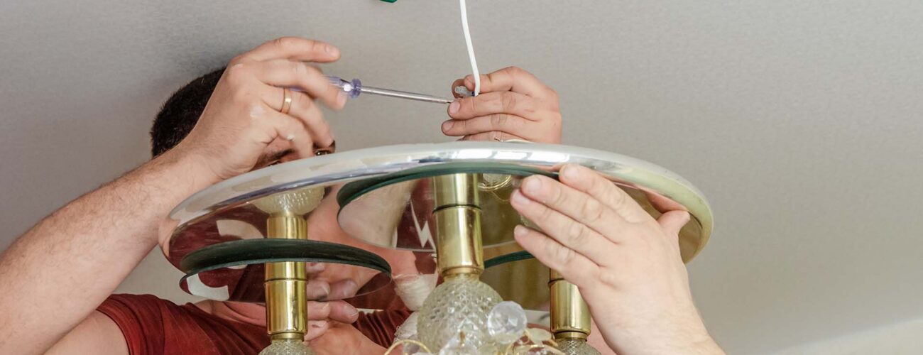 Men repair, install and remove the chandelier with a screwdriver in the house. Service for repair, installation and removal of chandeliers. Disassembled suspended chandelier with bare wires