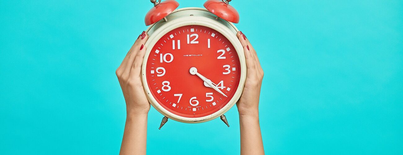 Person holding an alarm clock on a blue background