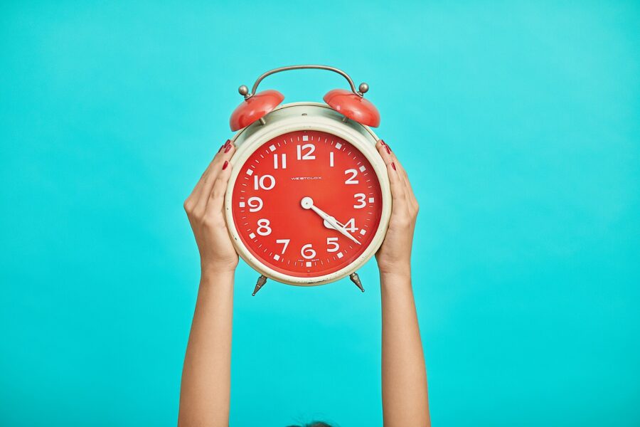 Person holding an alarm clock on a blue background