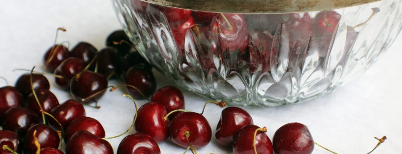 A glass bowl with cherries inside it and around it