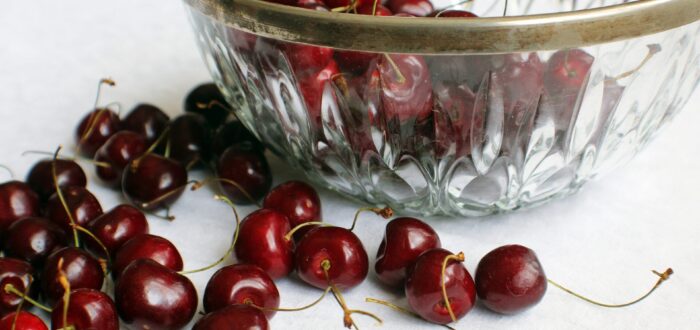 A glass bowl with cherries inside it and around it